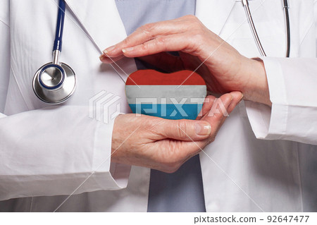 Doctor holding heart with flag of Grand Duchy of Luxembourg background. Healthcare, charity 92647477