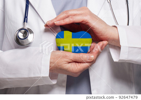 Swedish doctor holding heart with flag of Sweden background. Healthcare, charity Swedish doctor holding heart with flag of Sweden background. Healthcare, charity 92647479