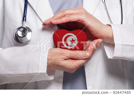 Tunisian doctor holding heart with flag of Tunisia background. Healthcare, charity 92647480