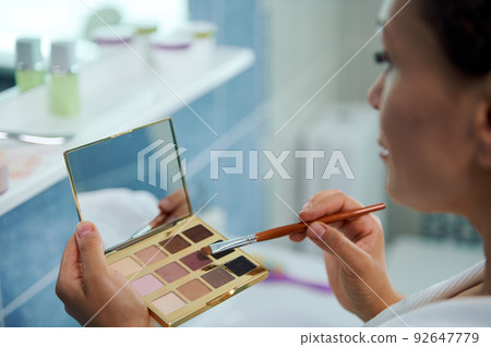 Soft focus on a beautiful eyeshadows palette and a make-up brush in the hands of blurred woman, applying make-up 92647779