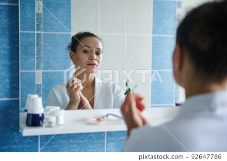 Reflection in the bathroom mirror of a serene woman massaging her hands soaked in moisturizer, caring for her hands skin 92647786