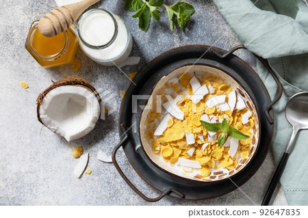 Summer vegan breakfast. Cereal granola breakfast flakes with coconut non-dairy alternative milk and fresh coconut slices on a stone tabletop. View from above. 92647835
