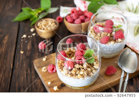 Healthy breakfast menu concept. Home made granola breakfast. Glass of parfait made of granola, berries raspberry, yogurt with chia seeds on rustic table. Copy space. 92647955