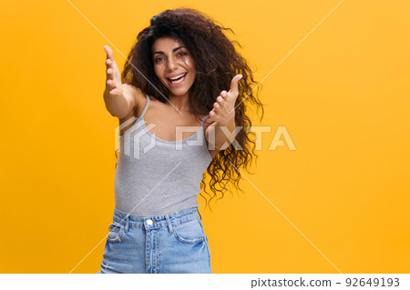 NICE TO MEET YOU. FRIENDLY HUGS CONCEPT. Enjoyed pretty Latin female with afro reach for camera, smile to you, stay isolated over yellow background. Copy space, free place NICE TO MEET YOU. FRIENDLY HUGS CONCEPT. Enjoyed pretty Latin female with afro reach for camera, smile to you, stay isolated over yellow background. Copy space, free place 92649193