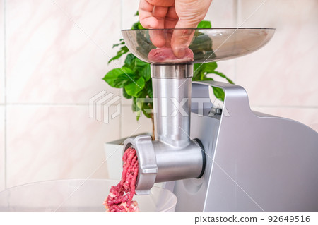 A man puts piece meat into electric meat grinder 92649516