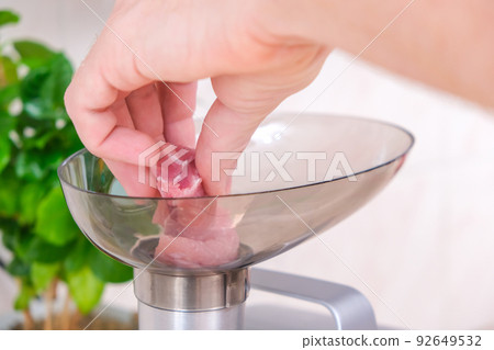 A man puts piece meat into electric meat grinder 92649532