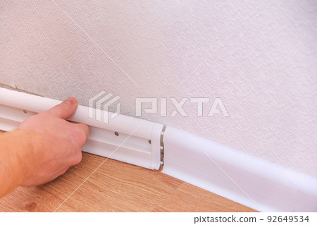 A man installs a floor skirting board. Fixing the A man installs a floor skirting board. Fixing the 92649534