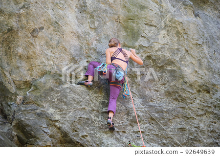 Young woman climbing steep wall of rocky mountain. Girl climber overcomes challenging route. Engaging in extreme sport concept. Young woman climbing steep wall of rocky mountain. Girl climber overcomes challenging route. Engaging in extreme sport concept. 92649639