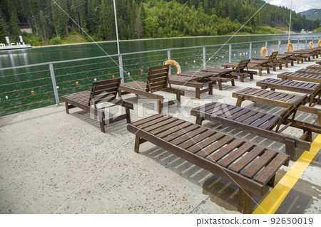 Row of empty wooden beach chairs near water. Row of empty wooden beach chairs near water. 92650019