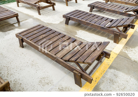 Row of empty wooden beach chairs near water outdoors. Row of empty wooden beach chairs near water outdoors. 92650020