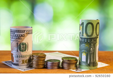One hundred euro and one hundred US dollar rolled bills banknotes, with euro coins and american cents on green blurred bokeh background. 92650160