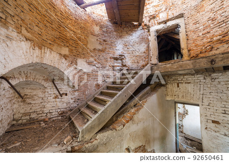 Large spacious forsaken empty basement room of ancient building or palace with cracked plastered brick walls, dirty floor and wooden staircase ladder. 92650461