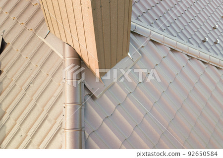 Detail view of house rooftop covered with brown metal tile sheets. Detail view of house rooftop covered with brown metal tile sheets. 92650584