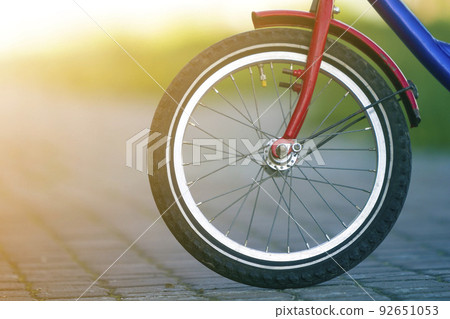 Close-up detail of teenager bicycle front wheel on gray pavement blurred bokeh background on bright sunny day. Urban comfortable transportation, speed, adventures and active lifestyle concept. 92651053