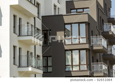 Close-up detail of apartment building wall with balconies and shiny windows on blue sky background. 92651064