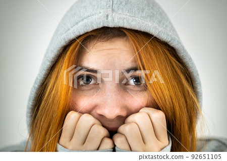 Close up portrait of scared young redhead woman wearing warm hoodie pullover. 92651105