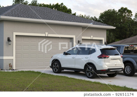Car parked in front of wide garage double door on concrete driveway of new modern american house 92651174