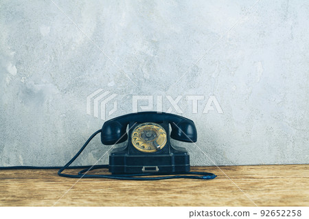 Retro black rotary telephone on wooden table in front gray concrete background Retro black rotary telephone on wooden table in front gray concrete background 92652258