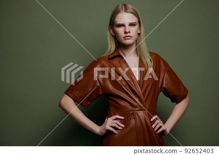 Women's Day concept. Stylish fashion self-confident young blonde woman holding hands on waist posing isolated on over olive green wall background looks at camera. Fashion offer for brands banner Women's Day concept. Stylish fashion self-confident young blonde woman holding hands on waist posing isolated on over olive green wall background looks at camera. Fashion offer for brands banner 92652403
