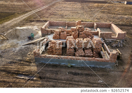 Aerial view of building site. Trenches dug in ground and filled with cement as foundation for future house, brick basement floor and stacks of brick for construction. 92652574