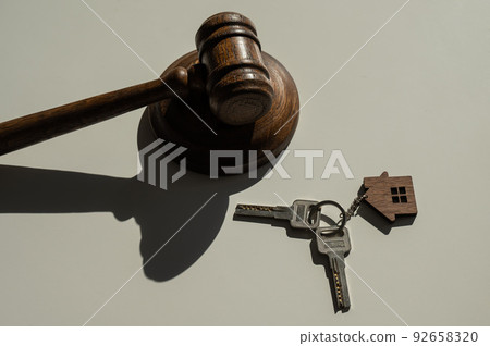 Keys with a keychain in the shape of a house and a judge's gavel on a white background. Keys with a keychain in the shape of a house and a judge's gavel on a white background. 92658320