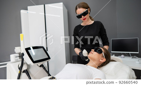 Young caucasian woman in goggles on photorejuvenation procedure. Doctor cosmetologist with a female patient. 92660540