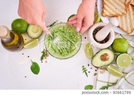 Woman mashing avocados in a glass bowl with a fork to prepare toasts Woman mashing avocados in a glass bowl with a fork to prepare toasts 92661799