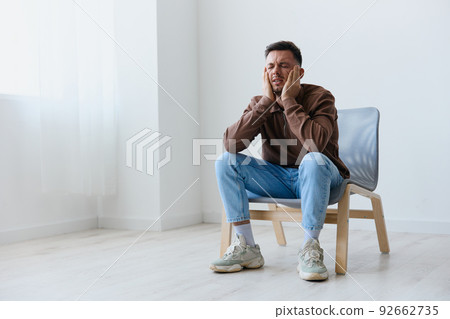 Sleepy tired upset unhappy young man touch head both hands closes eyes suffering from headache migraine sleeplessness sitting on chair at home. Mental problems Depression concept. Copy space Sleepy tired upset unhappy young man touch head both hands closes eyes suffering from headache migraine sleeplessness sitting on chair at home. Mental problems Depression concept. Copy space 92662735