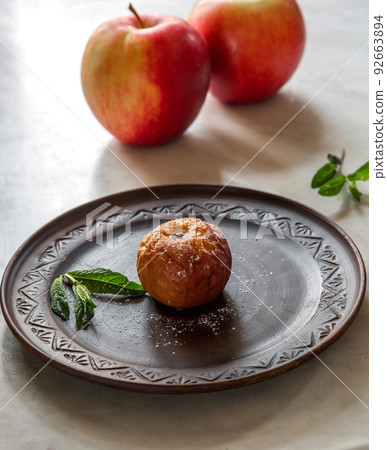 Baked apple on a brown plate with mint leaves and powdered sugar 92663894