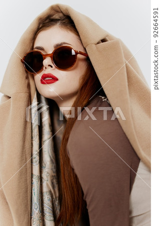 A red-haired girl with glasses and a coat on her head poses looking away. Banner for fashion design of a clothing store A red-haired girl with glasses and a coat on her head poses looking away. Banner for fashion design of a clothing store 92664591