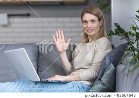 Woman sitting at home on the couch in the kitchen, using a laptop for a video call, talking to friends remotely Woman sitting at home on the couch in the kitchen, using a laptop for a video call, talking to friends remotely 92664648