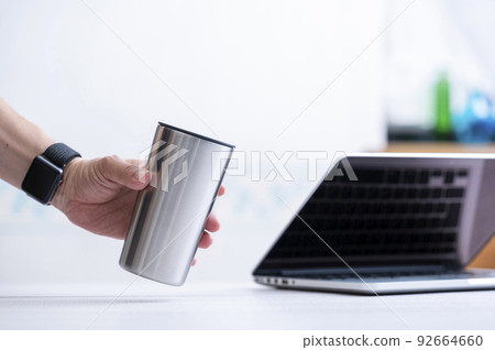 Male hand holding a stainless steel tumbler Male hand holding a stainless steel tumbler 92664660