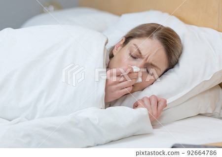 Close-up photo of a sick woman lying under a blanket in bed at home, has a runny nose and cold 92664786