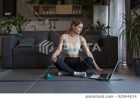 A middle-aged woman at home, engaged in fitness and fog, uses a laptop for online group activities A middle-aged woman at home, engaged in fitness and fog, uses a laptop for online group activities 92664814