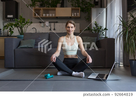 A middle-aged woman at home, engaged in fitness and fog, uses a laptop for online group activities 92664819