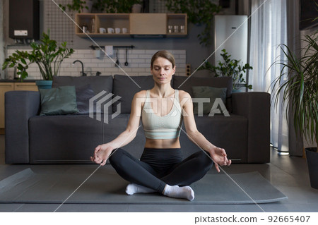 Woman at home sitting on the floor in the lotus position, meditating 92665407
