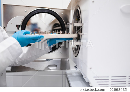 Close-up view of the hands of female dentistry worker who puts a dental instrument into autoclave. Sterilization of medical equipment 92668485