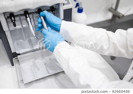 Close up of dental worker cleans and lubricates dental handpieces on a special machine Close up of dental worker cleans and lubricates dental handpieces on a special machine 92668486