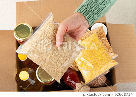 Plastic container with uncooked rice in female hand on emergency food box background 92668734
