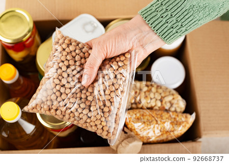 Plastic container with chickpeas in female hand on emergency food box background 92668737