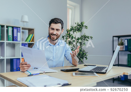 Happy businessman working with papers, working on laptop, man at work in a bright office Happy businessman working with papers, working on laptop, man at work in a bright office 92670250