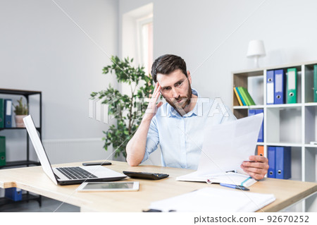 Frustrated and worried businessman looks at bad performance of the company on the documents, an evil man holds in his hands financial reports with errors Frustrated and worried businessman looks at bad performance of the company on the documents, an evil man holds in his hands financial reports with errors 92670252