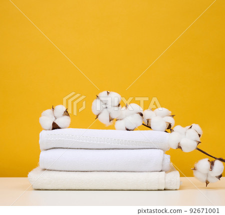 Twisted white terry towels on white table, yellow background Twisted white terry towels on white table, yellow background 92671001