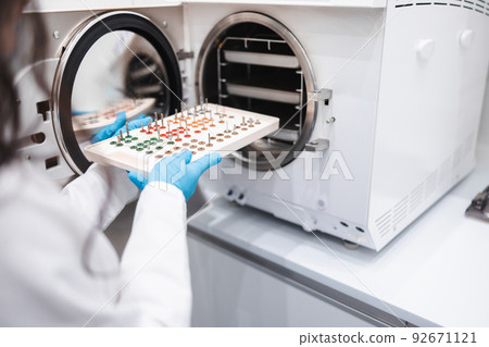 Close-up of a female dental assistant who puts a dental instrument into an autoclave. Concept of sanitary rules for dental treatment 92671121