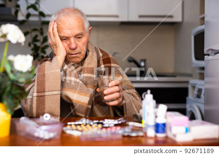 gray haired elderly man with handful of different medications in hand at home 92671189