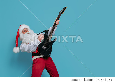 Emotional Santa Claus plays on electric guitar on color background. Christmas music. New Year party Emotional Santa Claus plays on electric guitar on color background. Christmas music. New Year party 92671463