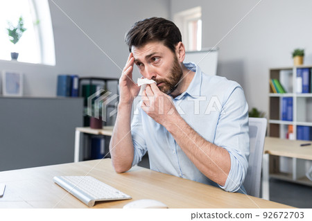 Businessman sick in the office man with allergies sneezes, sitting at a table with a computer 92672703