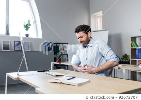 Sick man at work sitting at the table, has severe abdominal pain, businessman unhappy and upset Sick man at work sitting at the table, has severe abdominal pain, businessman unhappy and upset 92672707