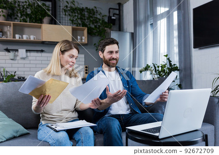 Happy married couple doing paperwork at home, calculating family budget and paying bills, using laptop, sitting on sofa at home Happy married couple doing paperwork at home, calculating family budget and paying bills, using laptop, sitting on sofa at home 92672709