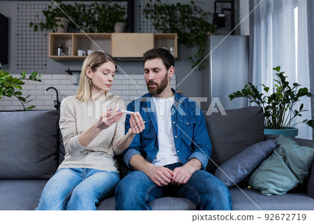 Sad man and woman sitting on the couch, disappointed with a negative pregnancy test Sad man and woman sitting on the couch, disappointed with a negative pregnancy test 92672719